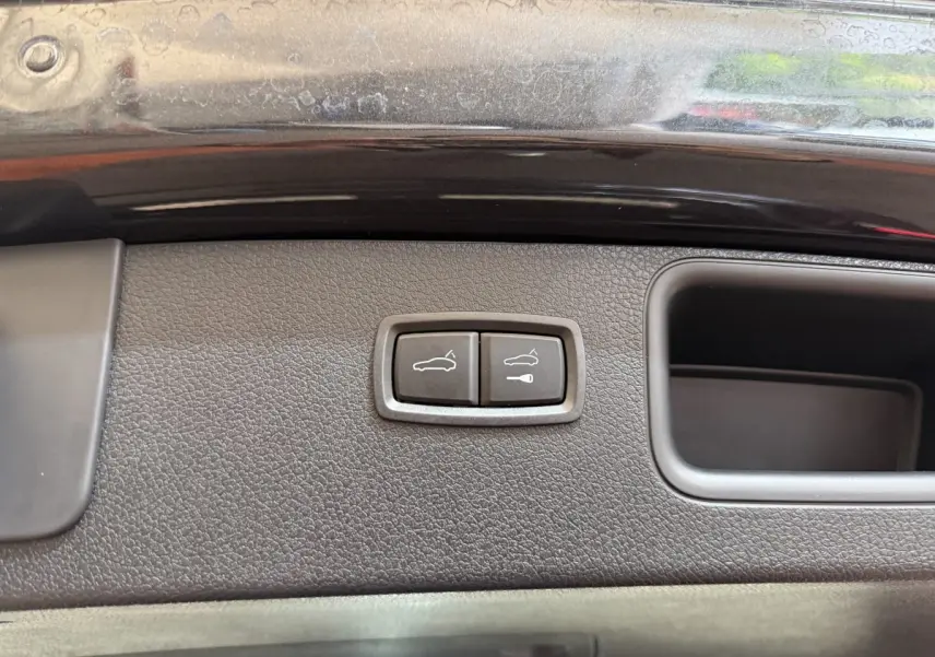 Gros plan sur les boutons d'ouverture électrique du coffre sur la porte arrière d'un Porsche Macan gris foncé.