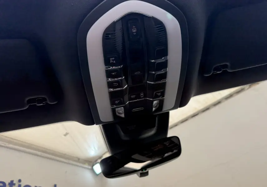 Vue en contre-plongée du panneau de commandes au plafond noir du Porsche Macan 3.0 S gris foncé, avec rétroviseur intérieur visible.