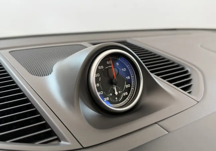 Gros plan sur l'horloge centrale du tableau de bord du Porsche Macan 3.0 S gris foncé, intérieur épuré et moderne.