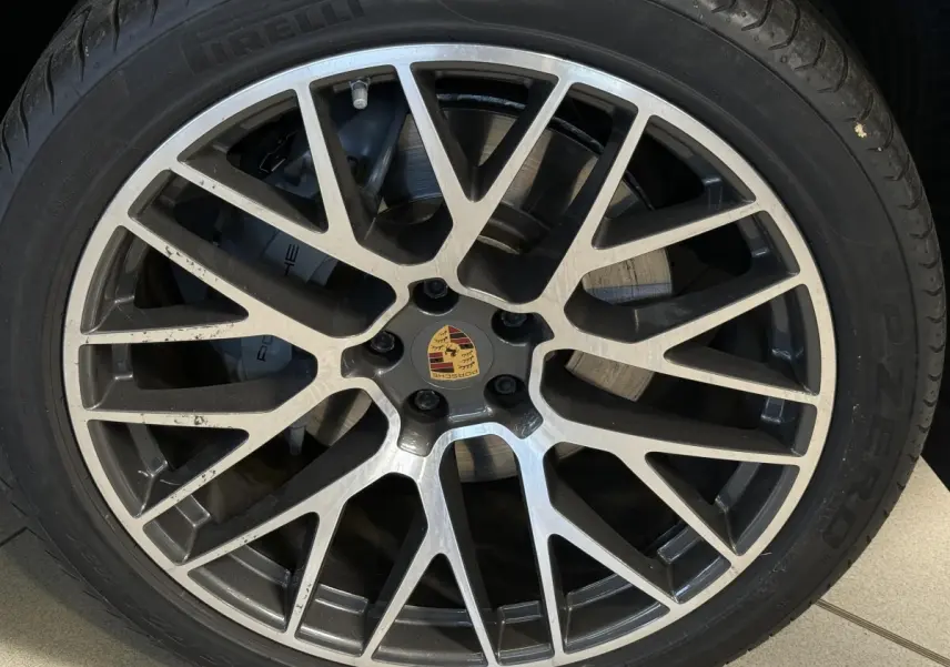Gros plan sur la jante alliage bicolore et le logo Porsche au centre du pneu Pirelli d’un Macan gris foncé.