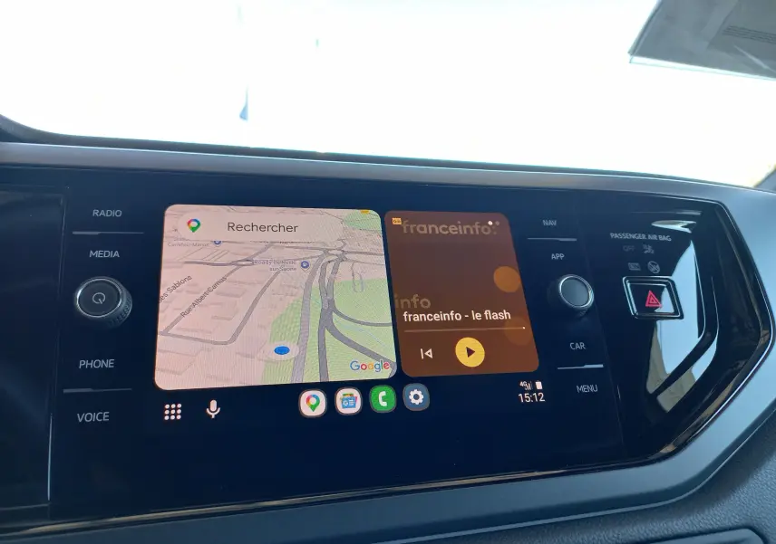 Écran tactile central de la Volkswagen Polo 2025 affichant navigation et radio, avec commandes autour et bouton d’alerte rouge.