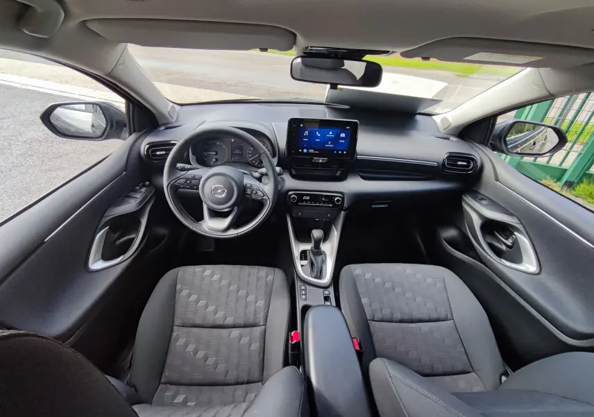 Vue intérieure avant de la Mazda2 2024 gris foncé, avec tableau de bord numérique et écran tactile central.