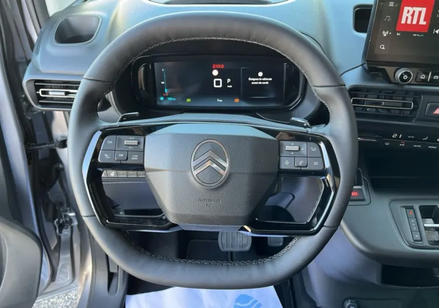Vue intérieure centrée sur le volant du Citroën Berlingo 2025 gris artense avec tableau de bord digital et commandes intégrées.