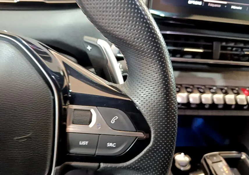 Gros plan sur le volant cuir perforé côté gauche du Peugeot 5008 Bleu, avec commandes audio et téléphone intégrées.