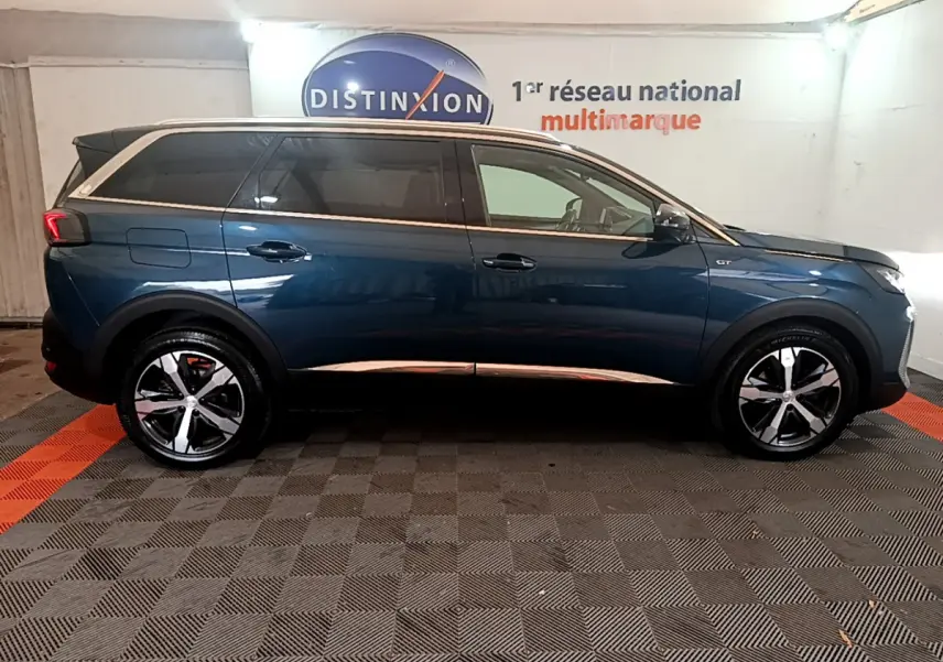 Profil droit d'un Peugeot 5008 GT bleu 2021 avec jantes alliage et toit contrasté blanc en intérieur showroom.
