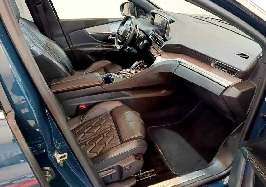 Intérieur côté conducteur du Peugeot 5008 bleu 2021, avec sièges cuir noirs et tableau de bord moderne tactile.