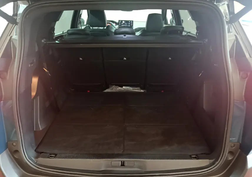 Coffre ouvert vu de l'arrière du Peugeot 5008 bleu, montrant la banquette rabattue et l'intérieur spacieux.