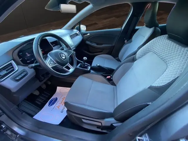 Vue intérieure côté conducteur de la Renault Clio V gris schiste, montrant les sièges textile gris et le volant avec tableau de bord numérique.