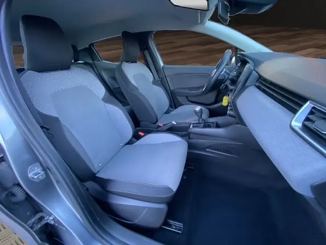 Vue intérieure côté conducteur de la Renault Clio V gris schiste, montrant les sièges textile gris et la console centrale avec boîte manuelle.
