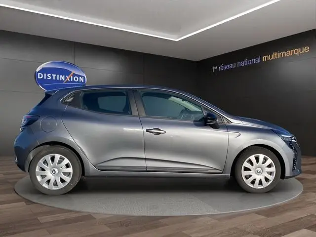 Profil droit d'une Renault Clio V gris schiste avec enjoliveurs 16 pouces, en présentation en showroom intérieur.