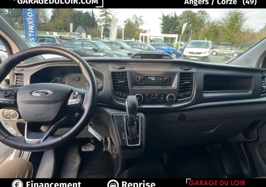 Vue intérieure avant du Ford Transit Custom blanc 2023, volant multifonctions en cuir et tableau de bord avec console centrale.