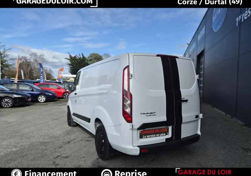 Vue 3/4 arrière droite du Ford Transit Custom blanc avec bande noire verticale centrale sur les portes arrière.