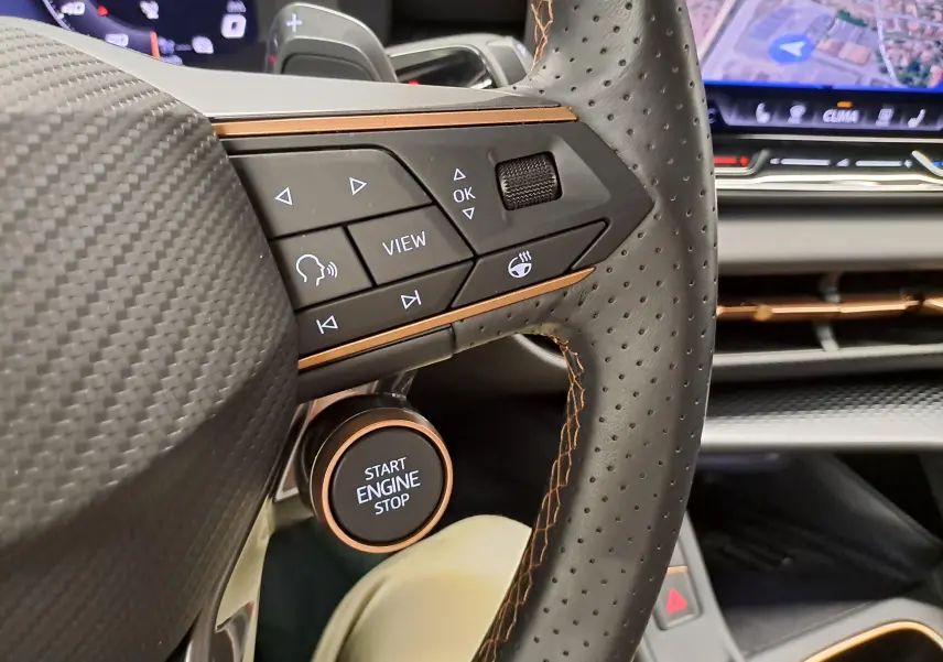 Gros plan sur le volant perforé noir avec surpiqûres orange du CUPRA Terramar 2025, bouton start engine visible.
