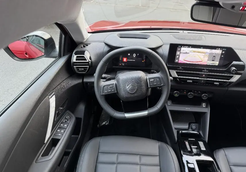 Vue intérieure avant du Citroën C4 rouge elixir 2025, tableau de bord avec écran tactile et volant multifonction.