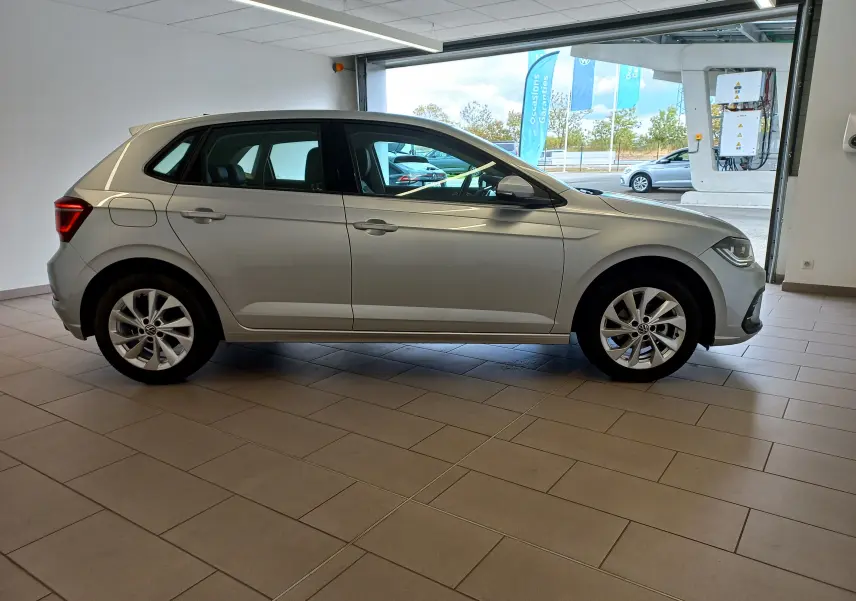 Vue de profil côté gauche d'une Volkswagen Polo 1.0 TSI 95 DSG7 Style en peinture reflet d'argent dans un showroom.