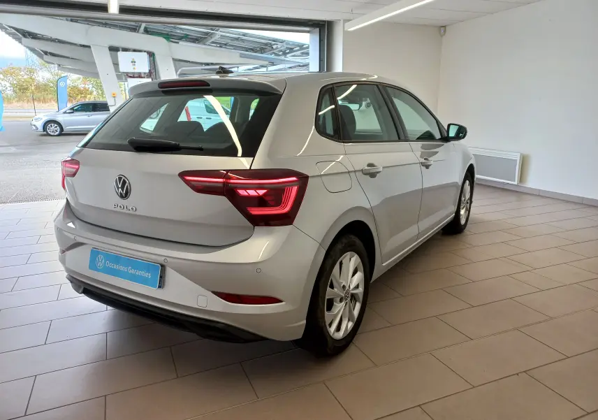 Vue 3/4 arrière droite d'une Volkswagen Polo 2026 couleur reflet d'argent avec feux arrière allumés en intérieur showroom.