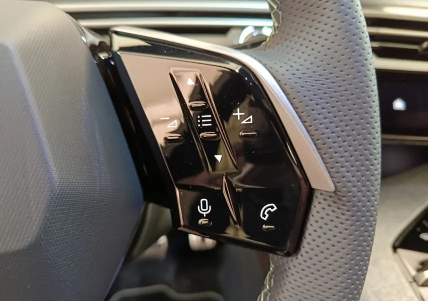 Gros plan sur les commandes vocales et téléphone intégrées au volant cuir perforé du Peugeot 3008 gris clair 2025.