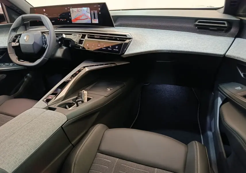 Intérieur du Peugeot 3008 2025, vue côté passager, tableau de bord gris clair avec écran tactile large et volant cuir noir.