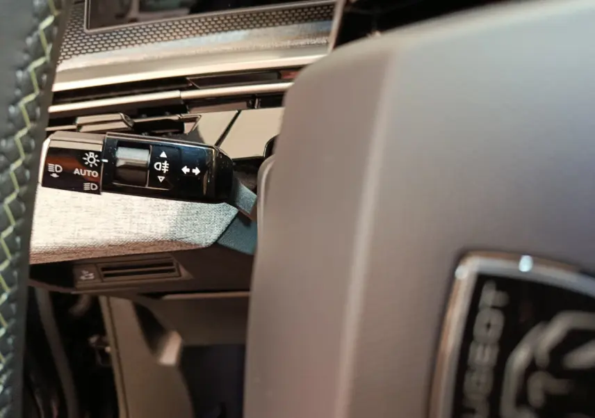 Gros plan sur la manette des feux à gauche du volant gris du Peugeot 3008 hybride 2025, intérieur moderne.