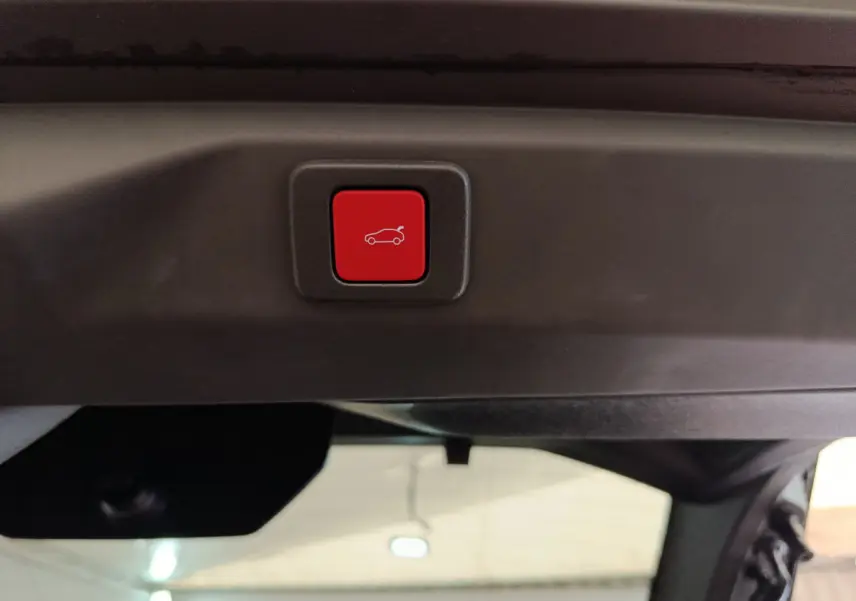 Bouton rouge de fermeture électrique du coffre sur la partie intérieure du hayon d'un Peugeot 3008 gris clair hybride 2025.