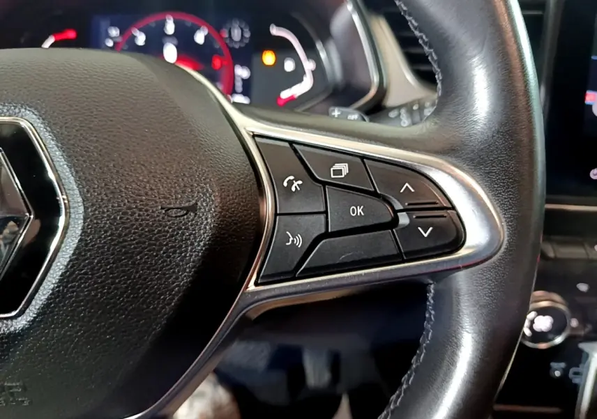 Gros plan sur la partie droite du volant cuir noir du Renault Captur jaune, avec commandes multifonctions et tableau de bord en arrière-plan.