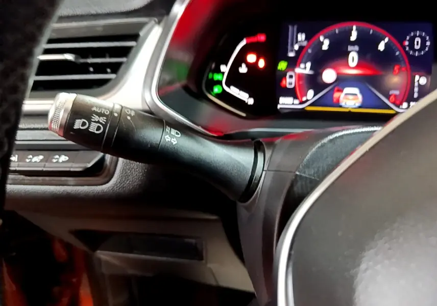 Gros plan sur la manette de commande des phares à gauche du volant avec tableau de bord numérique éclairé du Renault Captur jaune.