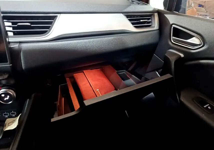 Vue intérieure côté passager du tableau de bord noir du Renault Captur Intens avec boîte à gants ouverte et rangement rouge visible.