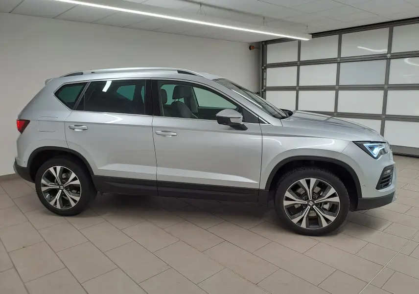Vue de profil côté gauche d'un SEAT Ateca 2025 argent métallisé avec jantes alliage 18 pouces dans un garage.
