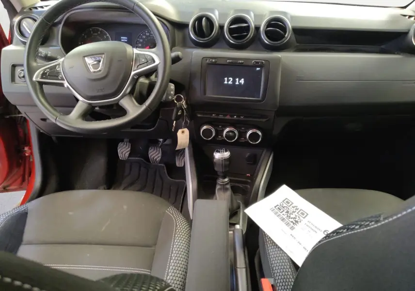 Vue intérieure avant du Dacia Duster rouge fusion 2021, montrant le volant, la console centrale avec écran tactile et levier de vitesses manuel.