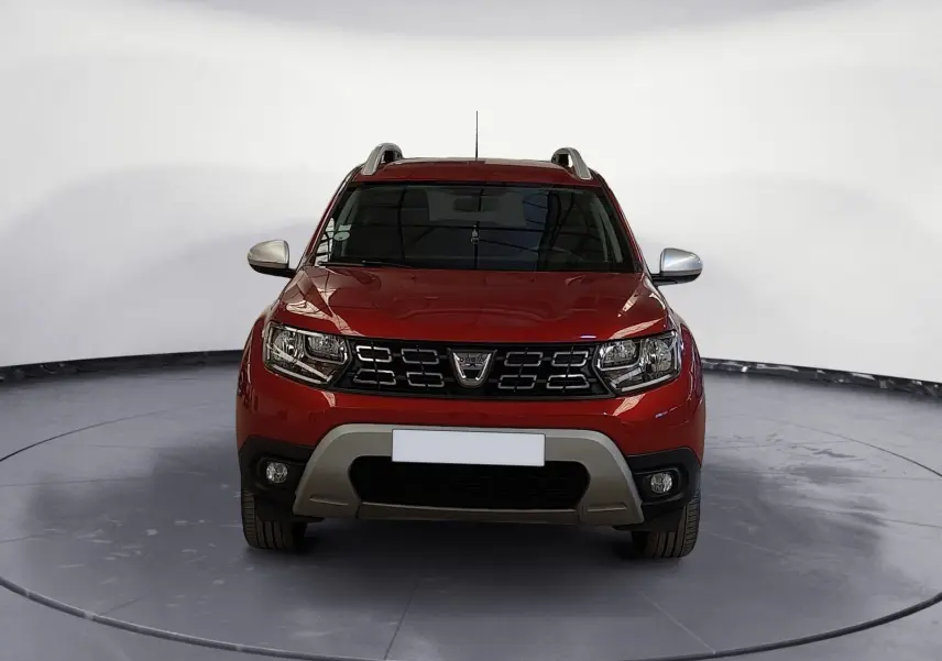 Vue frontale d'un Dacia Duster rouge fusion 2021 avec calandre noire et protections grises sous le pare-chocs.