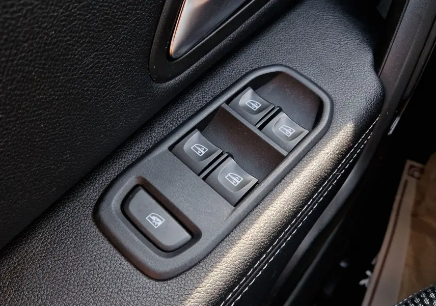 Gros plan sur les commandes de lève-vitres électriques côté conducteur du Dacia Duster 2021, finition noire avec surpiqûres blanches.