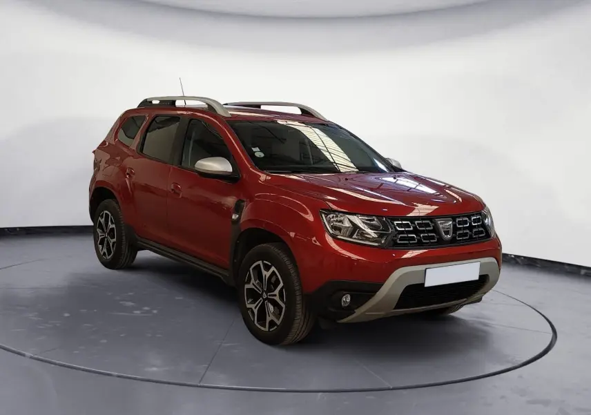 Dacia Duster rouge fusion en 3/4 avant droit, avec jantes alliage noires et barres de toit argentées.