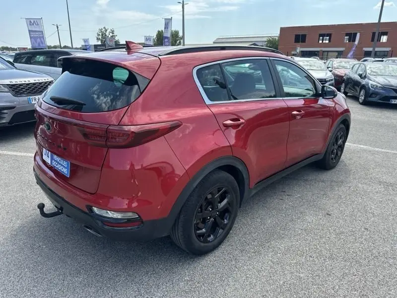 Vue 3/4 arrière droite d'un KIA SPORTAGE rouge métallisé 2021 avec jantes noires et attelage de remorque visible.