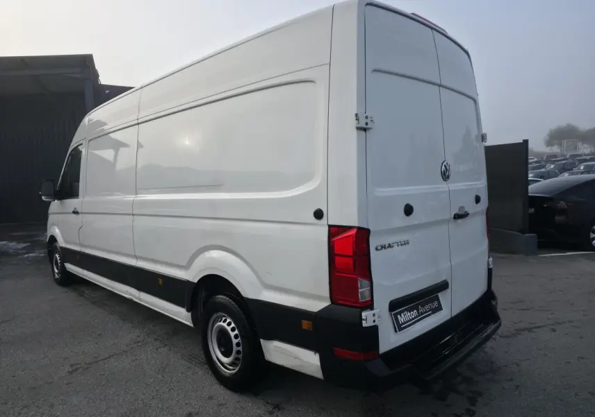 Vue 3/4 arrière droite d'un Volkswagen Crafter fourgon blanc avec jantes acier et bande noire latérale.