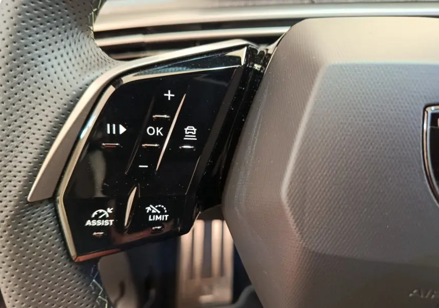 Gros plan sur les commandes gauche du volant cuir perforé du Peugeot 3008 blanc 1.2 HYBRID 145 E-DCS6 GT 2025.