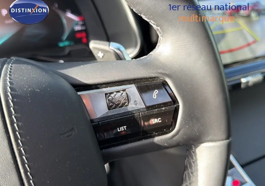 Gros plan sur les commandes au volant en cuir noir du DS7 1.5 BLUEHDI 130 EAT8 RIVOLI 2024, avec écran tactile en arrière-plan.