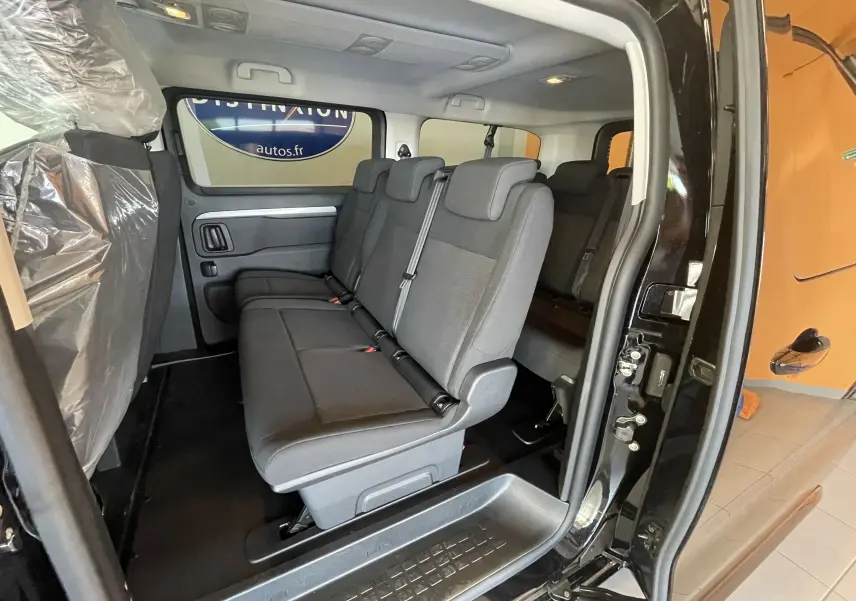 Vue intérieure côté droit du Peugeot Traveller noir 2026, montrant les sièges passagers en tissu et la porte coulissante ouverte.