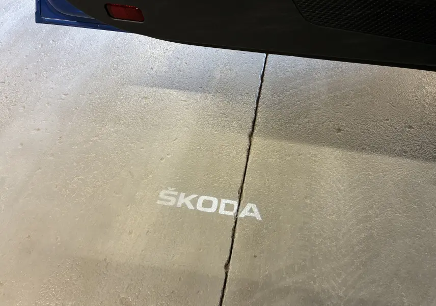 Projection lumineuse du logo SKODA au sol visible sous la porte ouverte d'une Octavia Combi bleue.