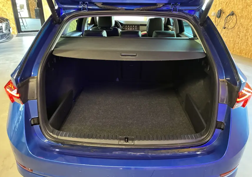 Vue arrière ouverte du coffre spacieux d'une Skoda Octavia Combi 2024 bleu, avec cache-bagages et intérieur noir visible.