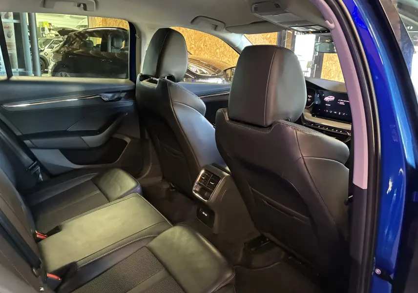 Vue intérieure arrière côté droit de la Skoda Octavia Combi bleu 2024 avec sièges en cuir noir et écran tactile avant visible.