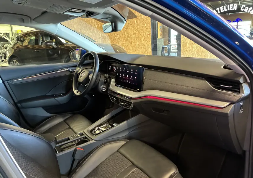 Vue intérieure côté conducteur de la Skoda Octavia Combi bleu 2024, avec tableau de bord moderne et éclairage d’ambiance rouge.