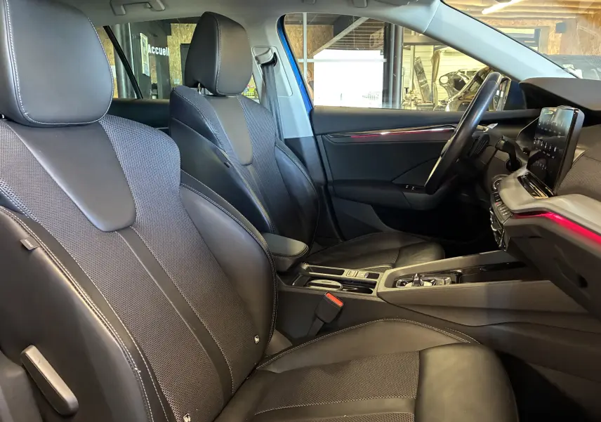 Vue intérieure côté conducteur de la Skoda Octavia Combi 2024 bleu, sièges tissu noir et tableau de bord moderne.