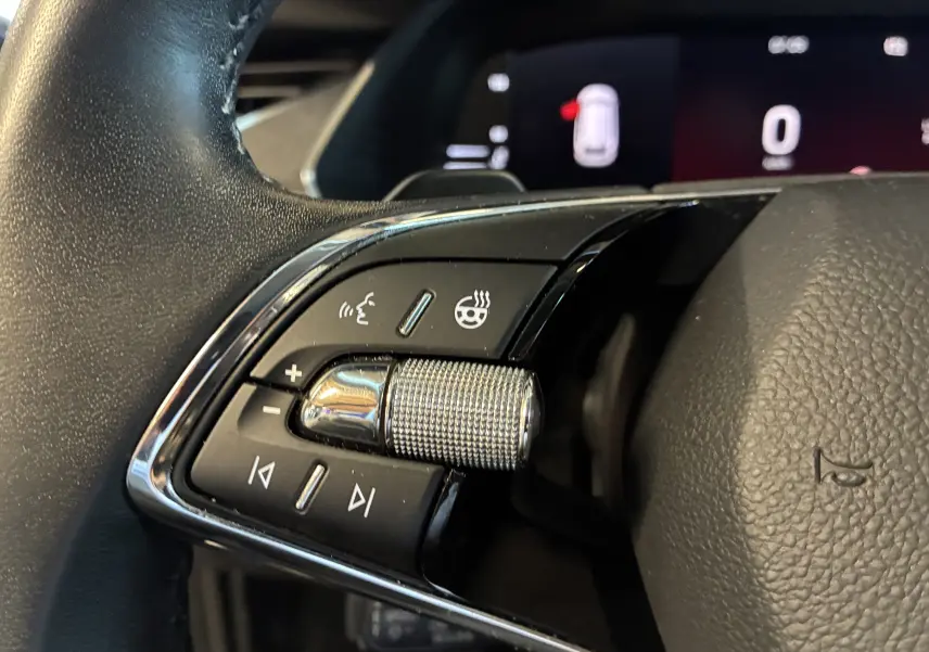 Gros plan sur les commandes gauche du volant noir de la Skoda Octavia Combi 2024, avec molette métallique texturée.