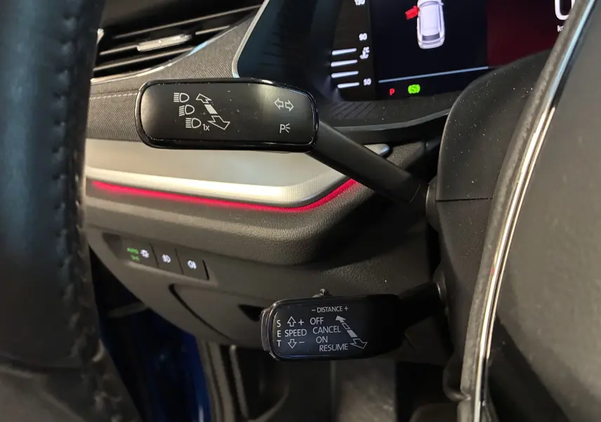 Gros plan sur les commandes au volant d’une Skoda Octavia Combi bleu 2024, avec éclairage d’ambiance rouge et tableau de bord numérique.