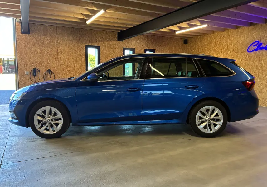 Vue de profil côté gauche d'une Skoda Octavia Combi 2024 bleu métallisé stationnée en intérieur avec jantes alliage.
