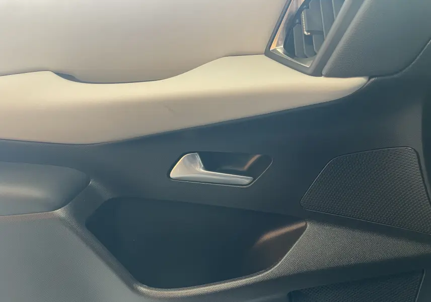 Gros plan sur la garniture intérieure côté droit du DS3 Crossback 2024, avec poignée argentée et panneau bicolore noir et beige.