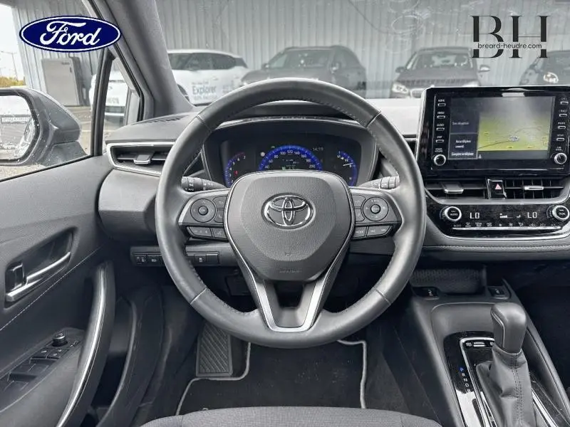 Vue intérieure centrée sur le volant cuir multifonction et l'écran tactile du tableau de bord d'une Toyota Corolla gris Manhattan.