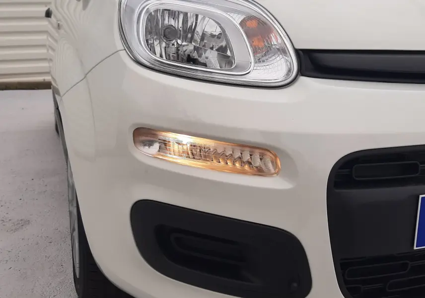 Gros plan sur l'avant gauche d'une Fiat Panda 2025 blanc gelato avec clignotant allumé et pare-chocs noir.