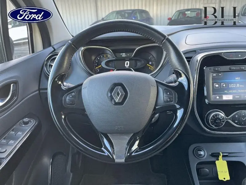 Vue rapprochée du volant cuir noir et tableau de bord digital d'une Renault Captur beige 2015 avec écran tactile central.