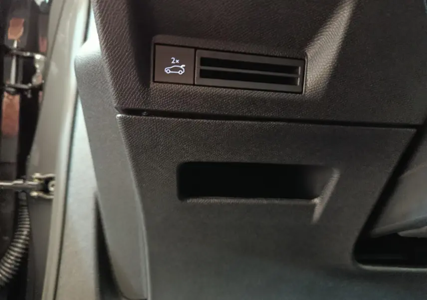 Détail du bouton d'ouverture du coffre sur la console côté conducteur du Peugeot 3008 noir hybride 2025.